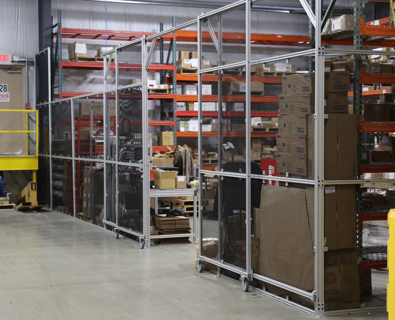 Modular T-slot aluminum machine guarding and safety enclosure with wire mesh panels and access doors protecting warehouse and manufacturing equipment while maintaining visibility and OSHA-compliant workplace safety.
