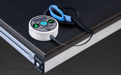 Professional ESD Wrist Strap with Continuous Grounding Monitor An ESD safety setup on an 80/20 aluminum workbench featuring a blue adjustable wrist strap connected to a white DESCO Mini Monitor with green LED status indicators, placed on a black static-dissipative work surface.