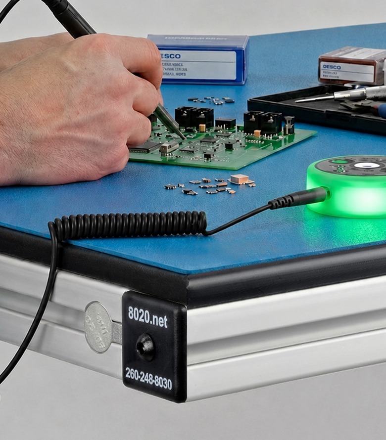 Modular Ergonomic Workstation with Static-Safe ESD Protection Horizontal banner of an 80/20 aluminum workstation featuring a blue ESD-safe table mat, a green-lit DESCO mini monitor, and an operator with a grounding wrist strap. An ESD Static-Safe logo is visible on the right.