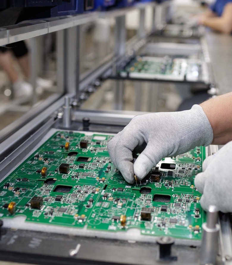 Electronics assembly worker at an ESD-compliant aluminum T-slot workstation placing component on PCB Worker wearing gloves placing an electronic component onto a green printed circuit board while working at an ESD-compliant aluminum T-slot workstation on a factory assembly line.