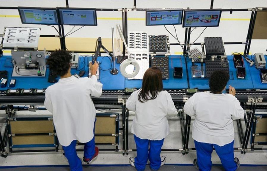 ESD-Safe Electronics Assembly Line with Ergonomic Workstations Technicians working at an ESD-safe electronics assembly line with ergonomic workstations, component trays, inspection tools, and digital monitors for electronics manufacturing and quality control.