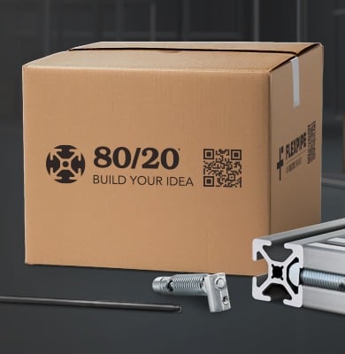 An 80/20 branded cardboard shipping box with the "Build Your Idea" logo and a QR code. In the foreground, a silver T-slot aluminum extrusion is shown with an anchor fastener and a hex key, demonstrating the modular assembly hardware included in a shipment