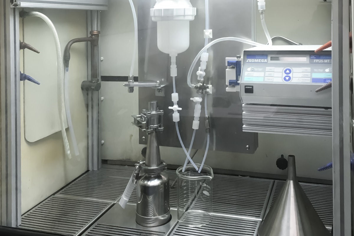 Stainless steel laboratory fluid handling and processing equipment with tubing, filtration components, and automated control unit inside a cleanroom workspace