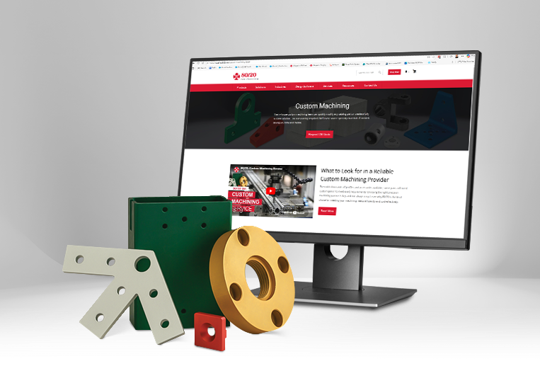 A desktop monitor displaying the 80/20 custom machining service webpage. In the foreground, physical examples of finished industrial parts are shown, including a yellow anodized circular component and various green and white powder-coated aluminum bracket