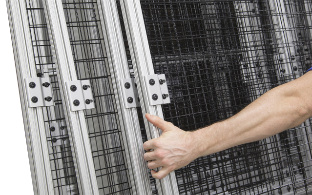 Close-up of a technician's hand moving a sliding safety partition made from 80/20 T-slot aluminum framing and black wire mesh infill panels. The assembly features heavy-duty aluminum hinges and modular hardware for industrial machine guarding and perimete