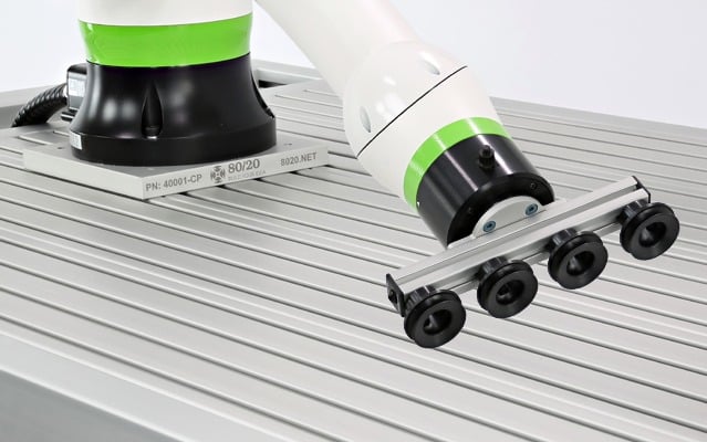 Collaborative robot arm equipped with a vacuum gripper handling materials on an aluminum extrusion workstation, demonstrating industrial automation and robotic material handling applications.