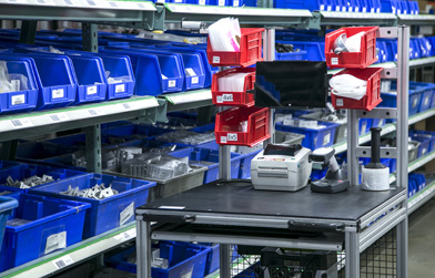 Efficient industrial storage system with blue bins and a workbench equipped with electronic devices and label printers.