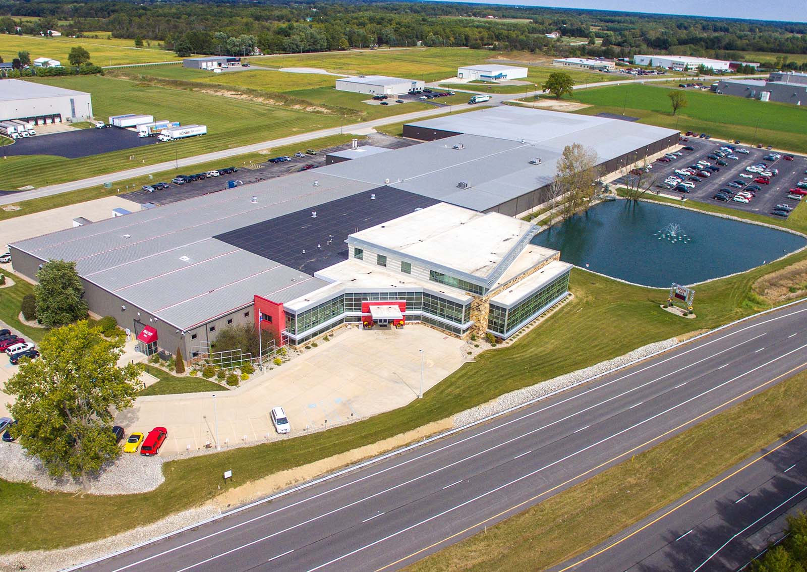 Aerial view of the 8020 building, featuring a modern commercial design with a red entrance and adjacent pond.