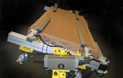 Custom clamping mechanism using aluminum extrusions holding a large cardboard package at an angle.
