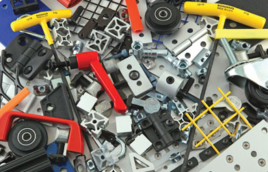 Assortment of industrial parts and tools, including yellow-handled screwdrivers, red clamps, black wheels, and metallic brackets on a blue surface.