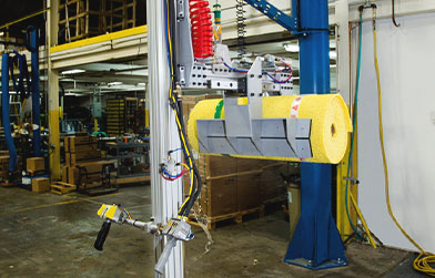 Industrial setting with a machine featuring a spool of yellow material and robotic handling equipment.