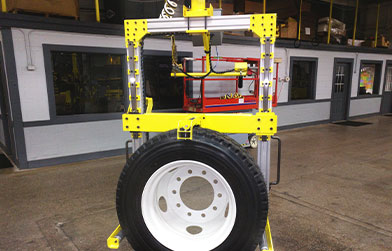 A yellow and red industrial lifting device in a workshop environment, with a large white tire attached.