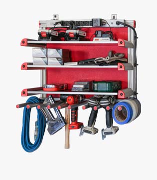 Wall-mounted tool organizer with shelves holding various power tools, hand tools, and hardware, with cords and tapes hanging below.
