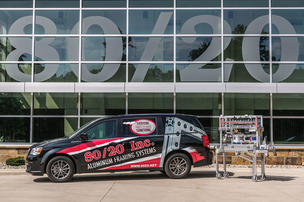 80/20 Inc. branded vehicle parked in front of a building with large windows reflecting the company's name, alongside an aluminum framing system.