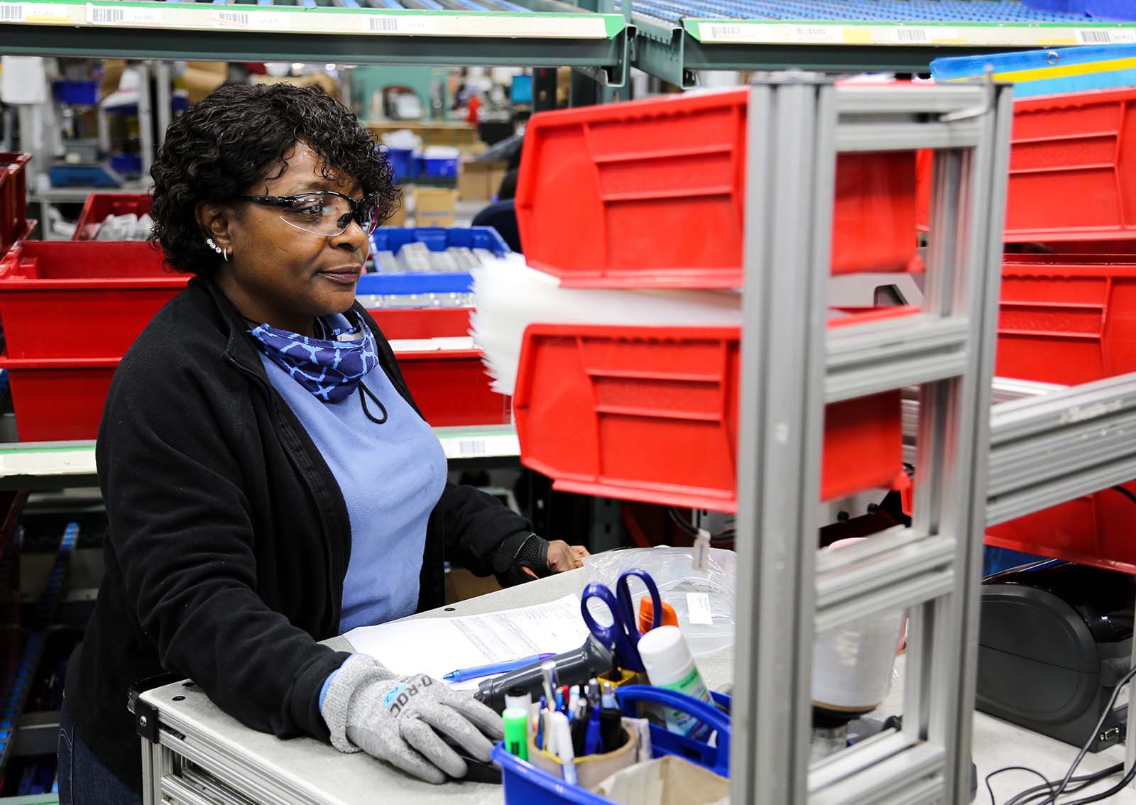 Worker at a manufacturing station with organizing bins and aluminum framing components.