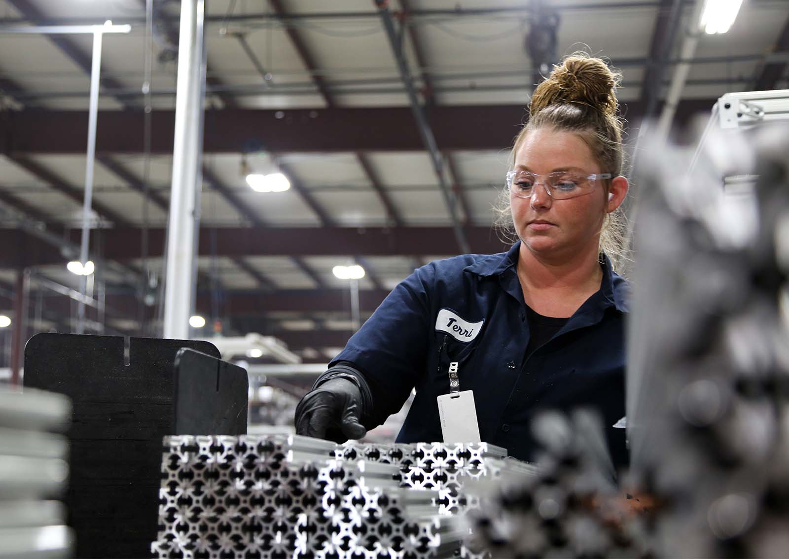 Female factory worker inspecting aluminum extrusions on the production line.