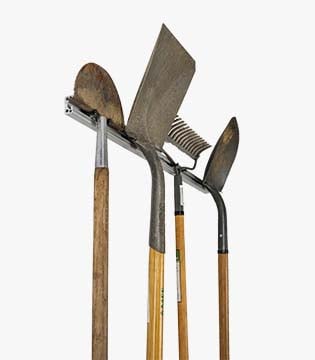 Wall-mounted tool rack holding garden tools, including shovels and a rake, with wooden handles and metal heads, isolated on a white background.